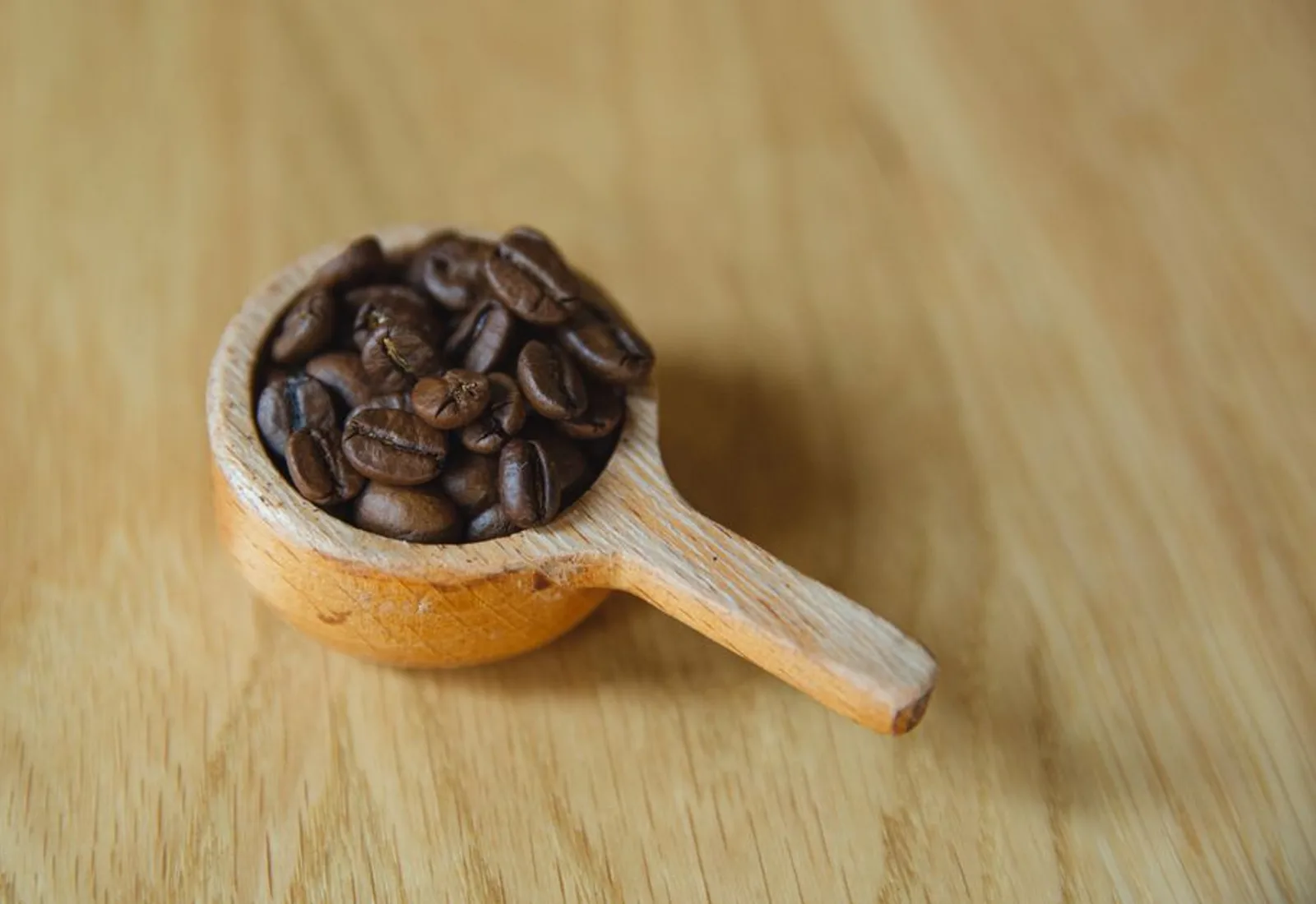 A wooden scoop of light-roast whole beans on a warm table