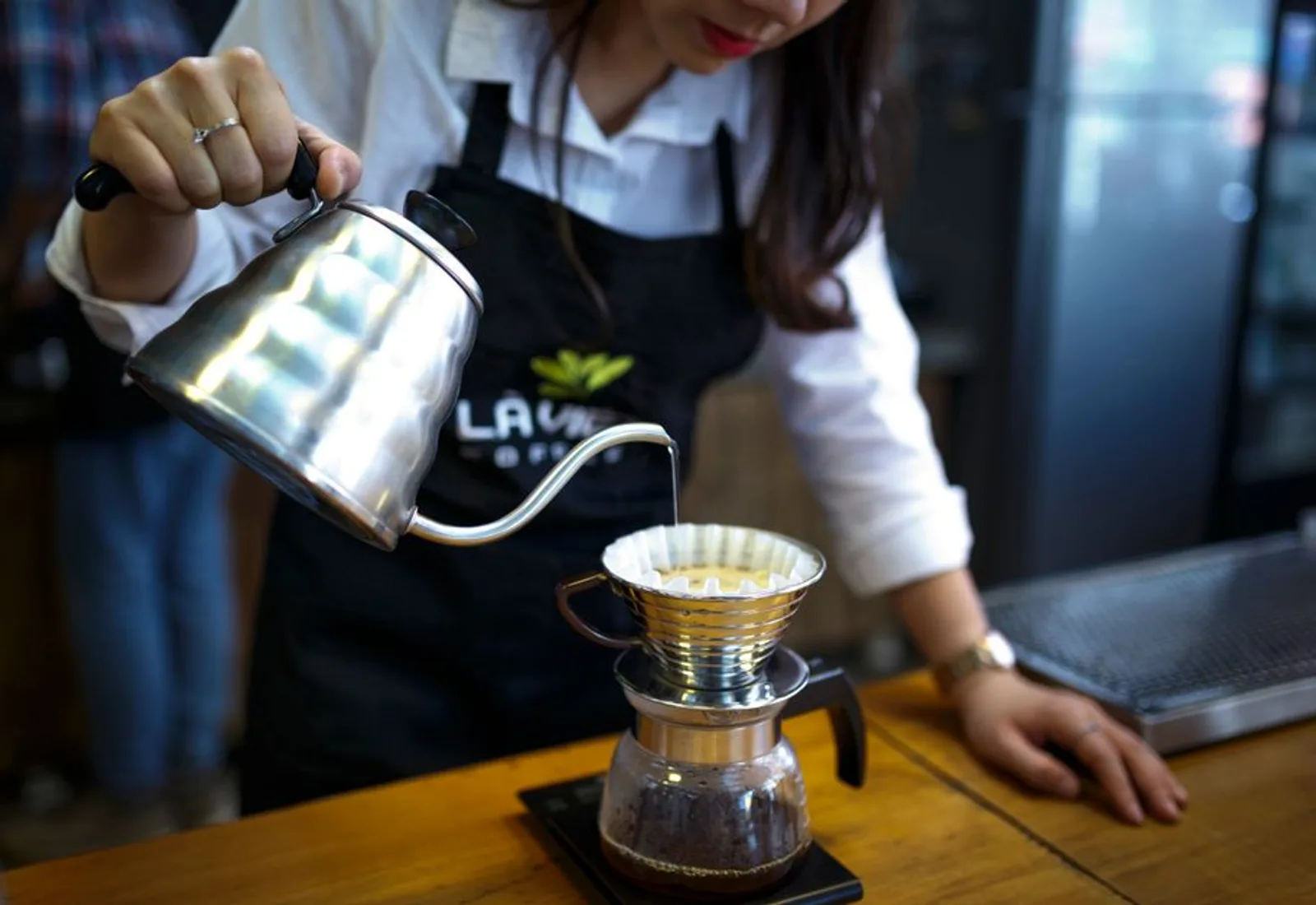 A barista pouring from a gooseneck kettle into a dripper