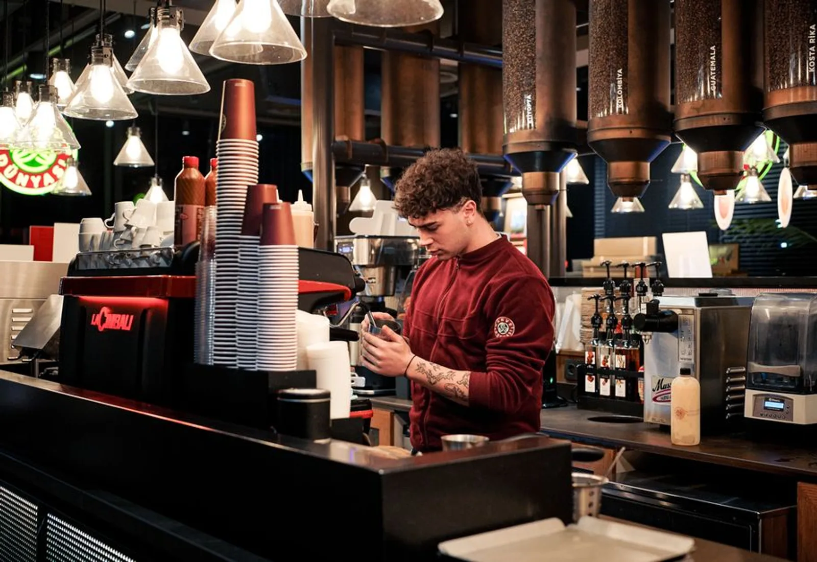 A barista working the espresso bar with bags of beans behind